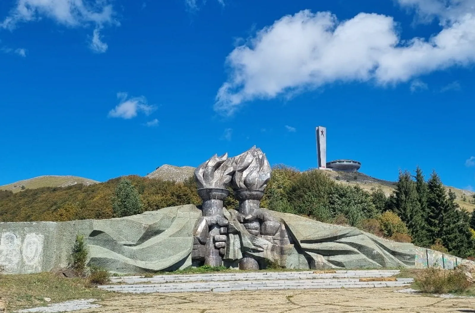 The UFO-shaped Buzludzha monument and its star-topped pylon on the ridge above the torch-bearing hands relief, central Bulgaria